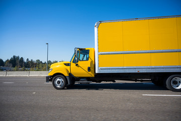 Fototapeta na wymiar Small rig yellow semi truck with long box trailer running on the highway in city limit