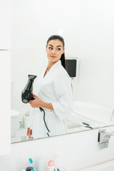 beautiful woman styling long hair with hairdryer in bathroom