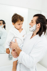 Obraz premium Dad holding toddler son at morning in bathroom