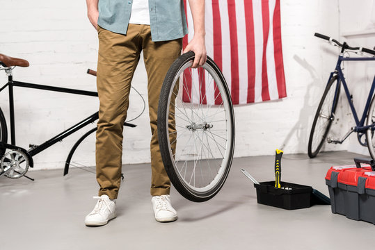 Cropped Image Of Man Holding Bicycle Wheel In Hand