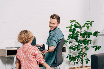 laughing man giving virtual reality headset to little son