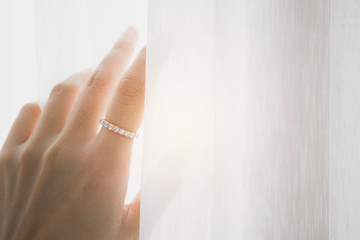 Close up of an elegant diamond ring on woman finger with white curtain and sunlight background....