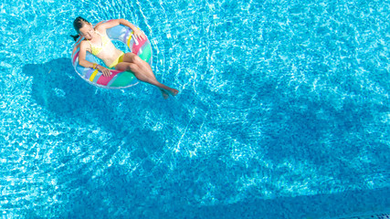 Aerial drone view of little girl in swimming pool from above, kid swims on inflatable ring donut , child has fun in blue water on family vacation resort
