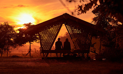 Romantic couple in love sitting together on terrace swing at sunset, silhouettes of young man and woman on holidays or honeymoon. Langkawi island, Malaysia.