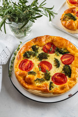 Vegetable pie quiche with broccoli, tomatoes and soft cheese on white background.