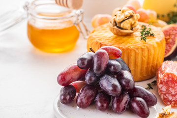 Cheese plate served with grapes, jam, figs, crackers and nuts on a background.