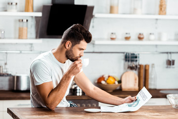 focused young man drinking coffee and reading newspaper in kitchen at morning