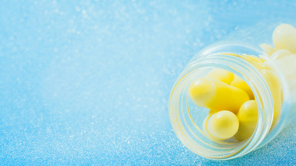 yellow capsules in a vial closeup on blue glitter, sparkles, sparkling background copy space. Global healthcare concept. Antibiotics drug resistance. Glimmer, sequins, bokeh effect.
