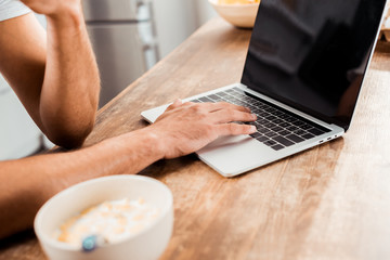 cropped shot of man using laptop with blank screen on kitchen table at morning