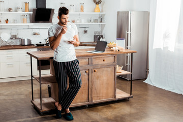 handsome young man in pajamas drinking coffee in kitchen