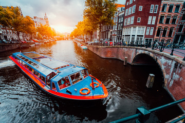 Ausflugsboot am berühmten holländischen Kanal am Sonnenuntergangsabend. Traditionelle holländische Brücken und mittelalterliche Häuser. Amsterdam Holland