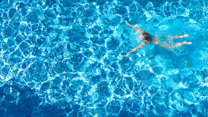 Active girl in swimming pool aerial drone view from above, young woman swims in blue water,...