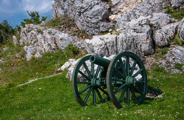 a gun standing next to a large stone on a green hill