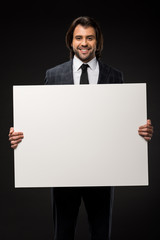 professional young businessman holding blank banner and smiling at camera isolated on black