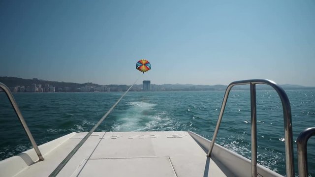 Excited tourists parasailing high in the sky, extreme sport, summer activities, POV from behind the yacht boat