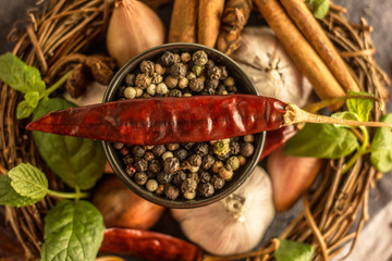 Mix of red, black and white pepper in a black bowl close-up against the background of chili pepper, garlic, cinnamon, onion and other spices
