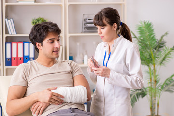 Young man with bandaged arm visiting female doctor traumatologis