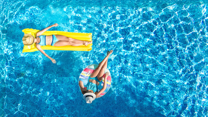 Aerial drone view of children in swimming pool from above, happy kids swim on inflatable ring donut and mattress, girls have fun in water on family vacation on holiday resort
