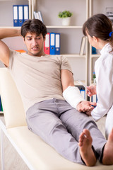 Fototapeta premium Young man with bandaged arm visiting female doctor traumatologis