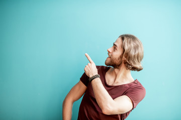 Portrait of a young caucasian bearded man with long hair dressed in t-shirt showing with hand on the colorful background