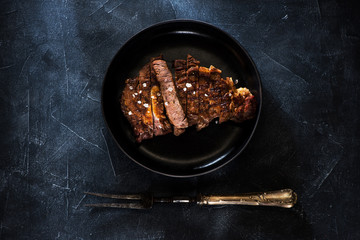 Grilled Steak ribeye Well Done on a plate and meat fork, top view