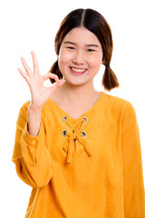 Studio shot of young happy Asian woman smiling while giving ok s