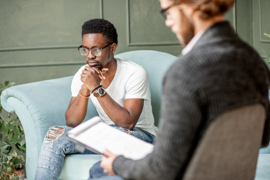Young afro ethnicity man having a serious conversation with psychologist sitting on the comfortable couch during psychological session in the office