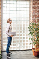 Portrait of a young caucasian businessman dressed casually standing near the wall with glass blocks indoors