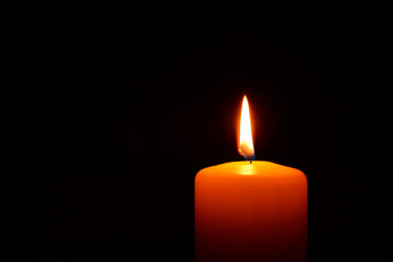 One orange candle flame  burning in darkness on black background with copy space for text.