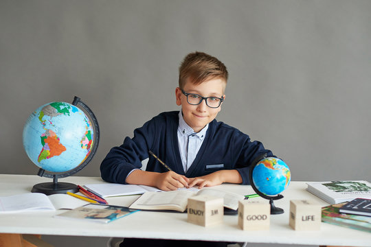 Back to school. Funny little schoolboy in glasses performs tasks. Child from elementary school with school supplies. Education and school concept. Distance learning.  Boy with globe