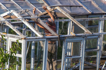 The old man repairs the greenhouse in the garden