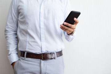 Closeup of business man holding and texting on smartphone. Entrepreneur standing and using digital gadget. Technology and communication concept. Cropped front view.