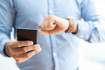 Closeup of business man holding smartphone and checking time. Entrepreneur using devices. Technology and appointment concept. Cropped front view.