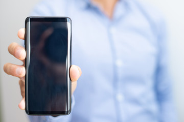 Closeup of man showing empty smartphone screen. Person holding digital device. Technology and promotion concept. Cropped front view.