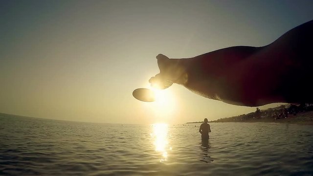 Hand is throwing a frisbee disc on beach on a summer sunset toned with a retro vintage instagram filter effect, SLOW MOTION