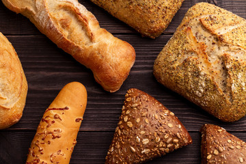 Contrast bread background. Concept for bakery menu. Different color, size and shape of the bread lies on the dark natural pine boards.