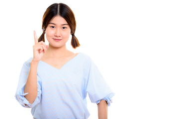 Studio shot of young beautiful Asian woman pointing finger up 
