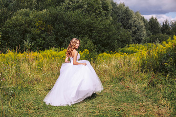 A cute young bride in a white dress is walking in the nature