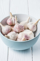 Blue ceramic bowl with garlic bulbs on white wooden table