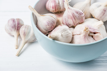 Garlic bulbs in blue ceramic bowl on white wooden table