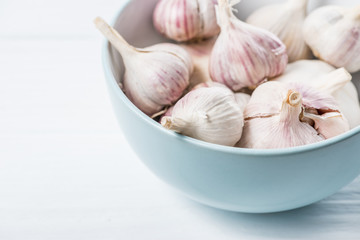 Garlic bulbs in blue ceramic bowl on white table