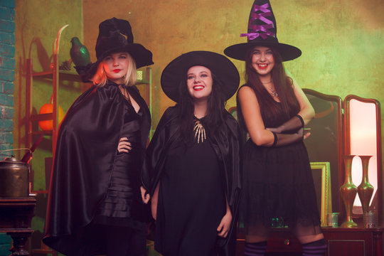 Photo of three witches in black hats in dark room against background of mirror