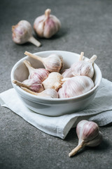 Garlic bulbs in ceramic bowl with white cloth on grey background