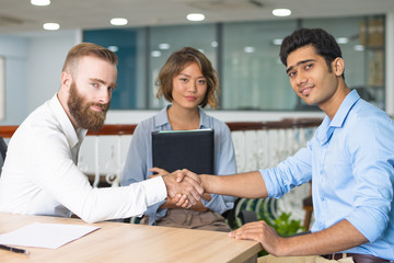 Fototapeta na wymiar Content Indian candidate shaking hands with company leader at and of job interview. Asian HR manager posing in background. Job interview concept