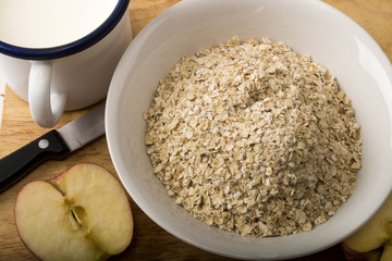 raw scottish oatmeal, milk in a mug and apple