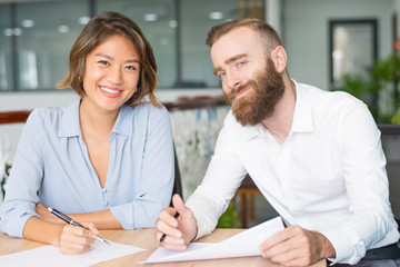 Happy successful professionals studying reports. Two colleagues posing while working at meeting table. Business consulting and expertise concept