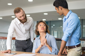 Young employee asking colleagues for help with report. Asian female manager talking to male...