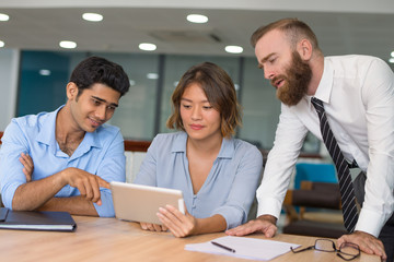 Young office employees testing and discussing new business app. Multiethnic group of three discussing content on tablet screen. Communication concept