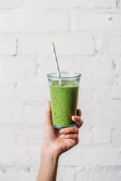 Female hand holding glass with green organic smoothie and straw
