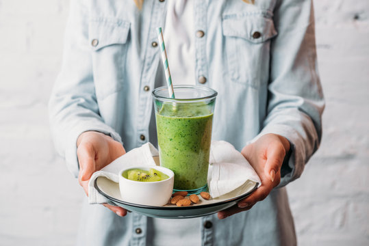 Female hands holding plate with glass of green smoothie and straw